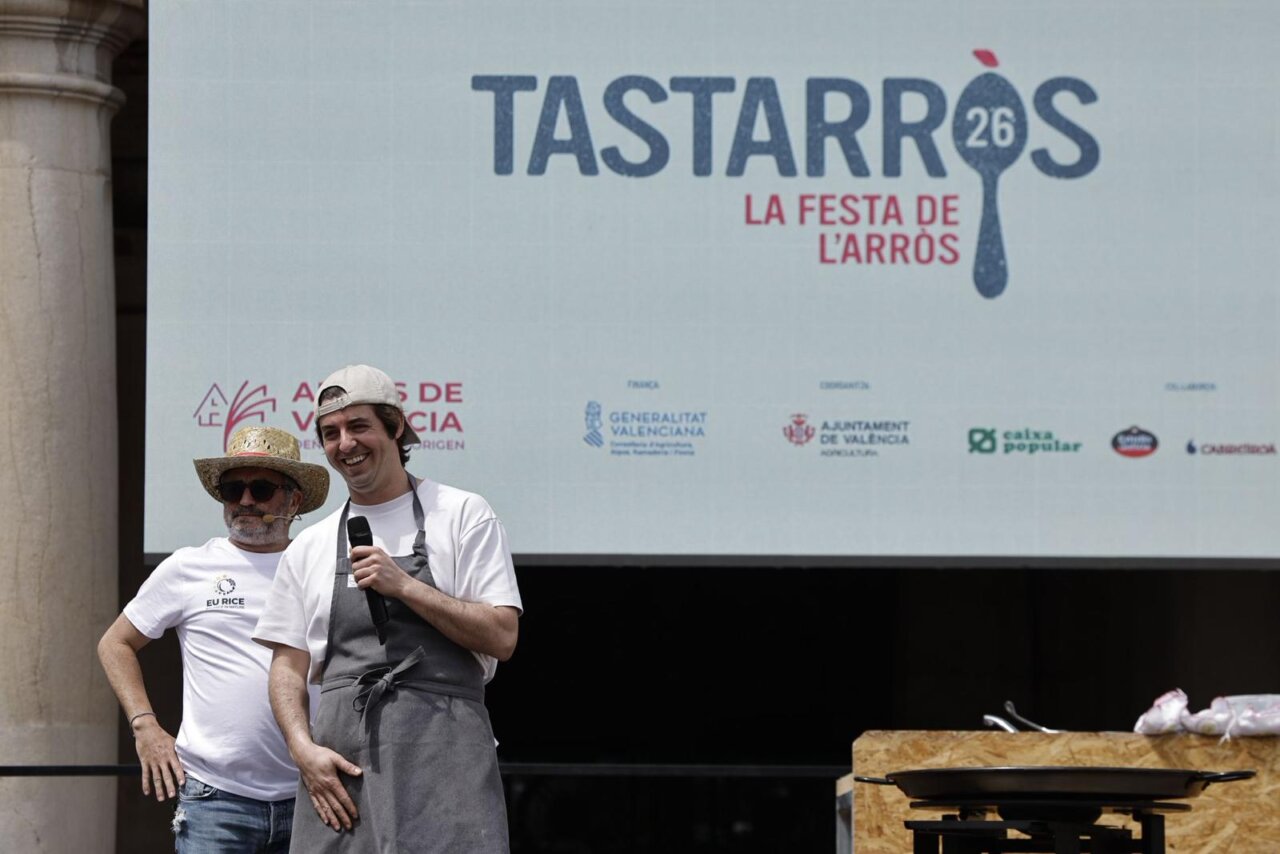 Dos chefs en el evento TastArròs en València, con un gran cartel detrás.