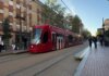 Tranvía de València circulando por la ciudad con pasajeros esperando en la parada.