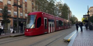 Tranvía de València circulando por la ciudad con pasajeros esperando en la parada.
