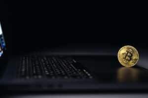 Bitcoin coin near laptop on black background. Finance and crypto money concept.