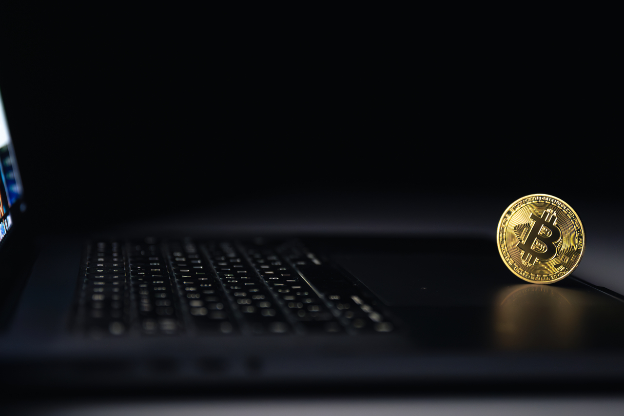 Bitcoin coin near laptop on black background. Finance and crypto money concept.