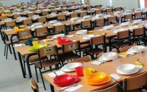 Mesas de comedor escolar preparadas con platos y utensilios coloridos