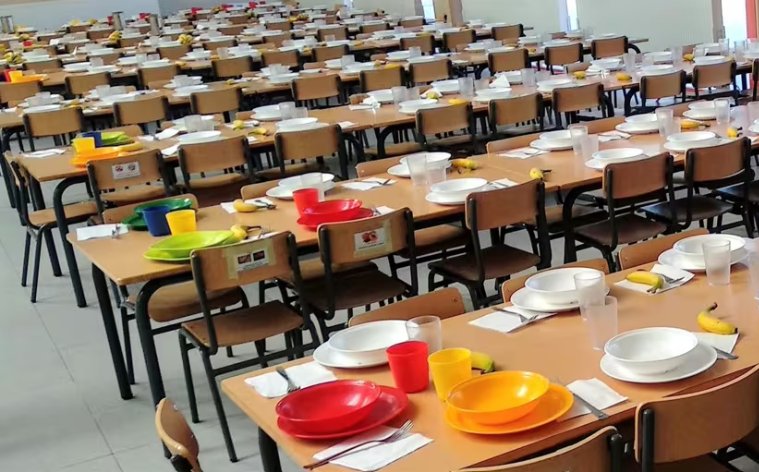 Mesas de comedor escolar preparadas con platos y utensilios coloridos