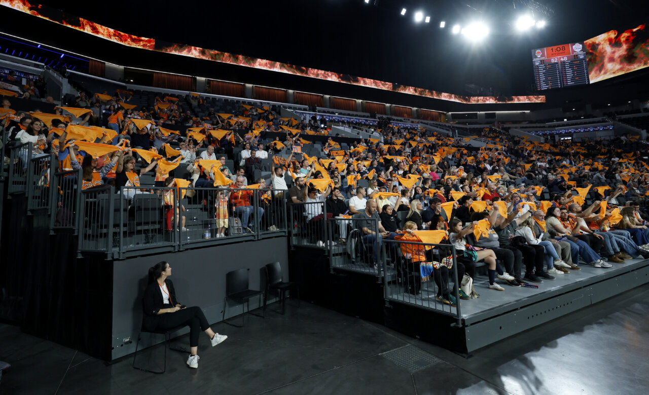 Aficionados de Valencia Basket animando con banderas naranjas en un partido