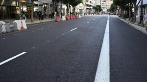 Calzada asfaltada con marcas viales, conos y barreras junto a comercios
