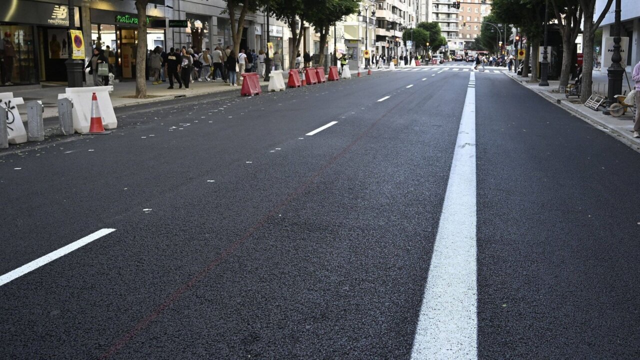 Calzada asfaltada con marcas viales, conos y barreras junto a comercios