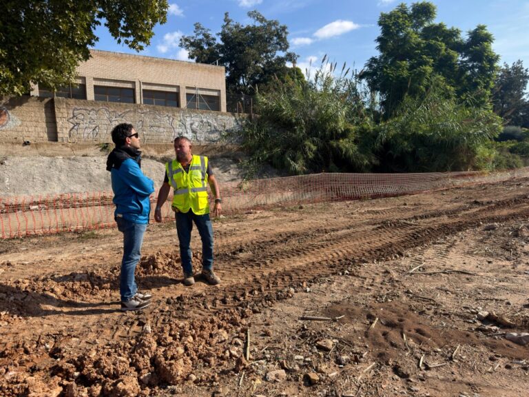 Dos hombres junto a terreno removido, con una malla naranja delimitando la zona de obras.